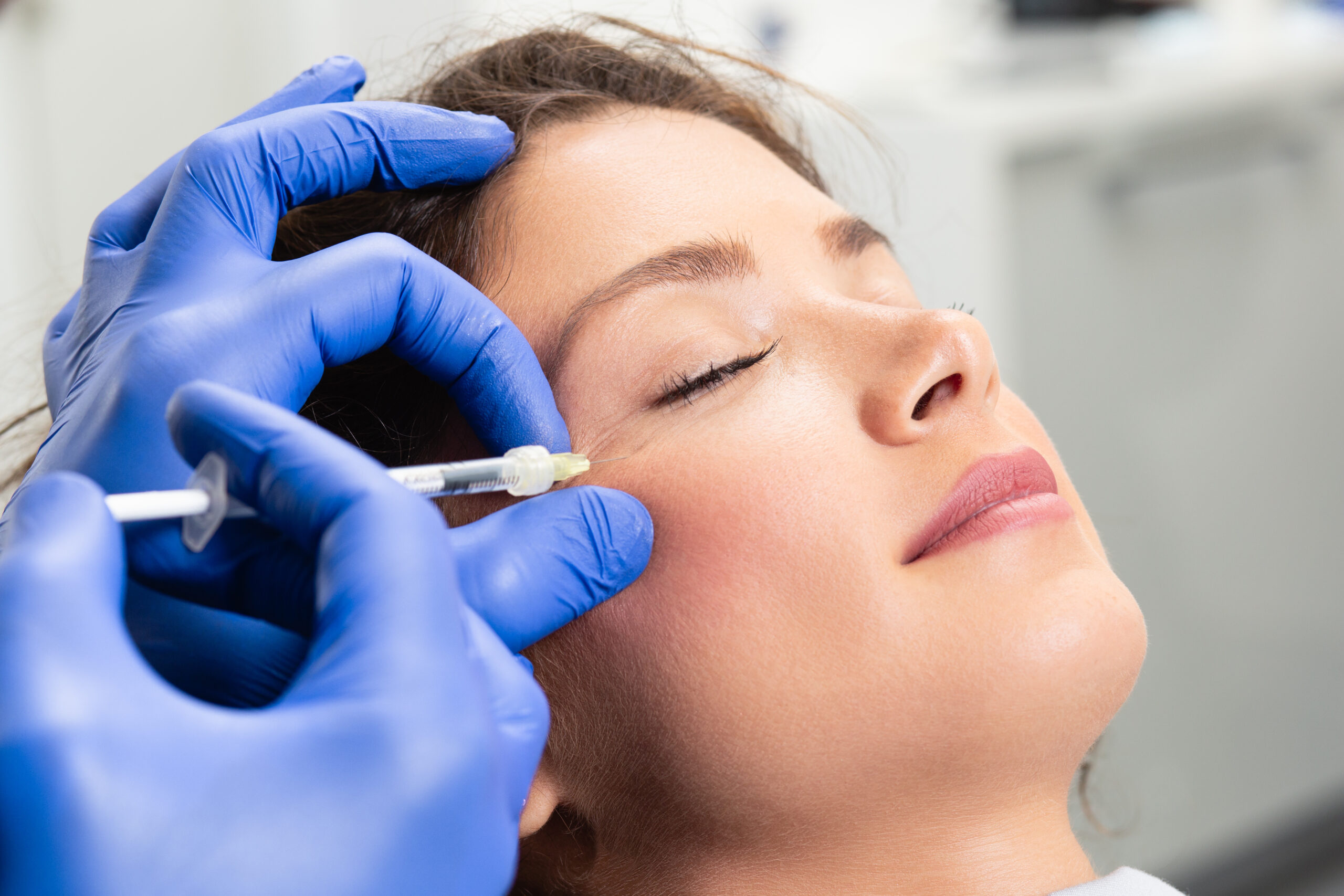 Practitioner administering an injectable treatment near a woman’s outer eye area while she rests with eyes closed.