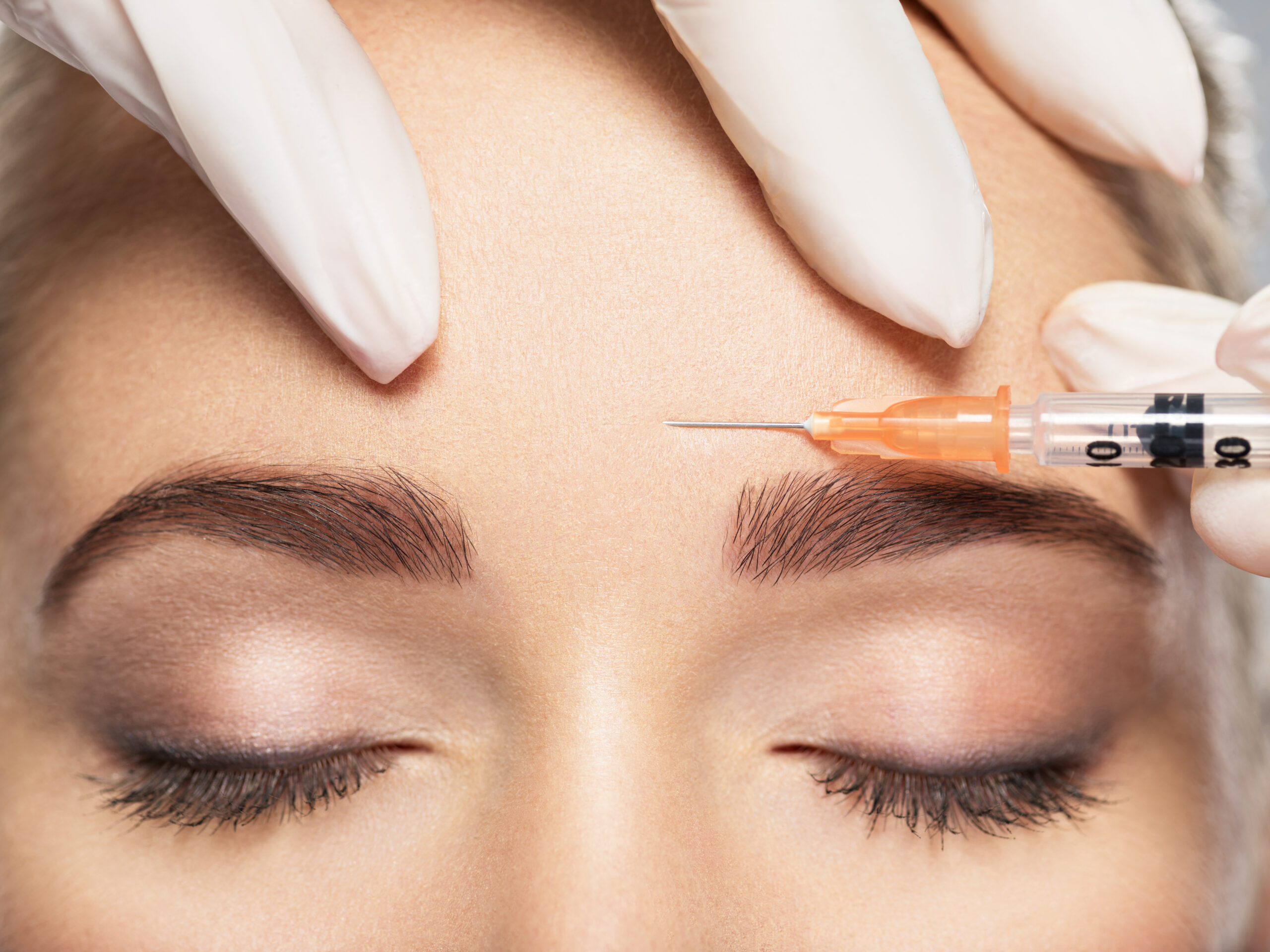 Close-up of a practitioner administering a Botox injection into a woman’s forehead.