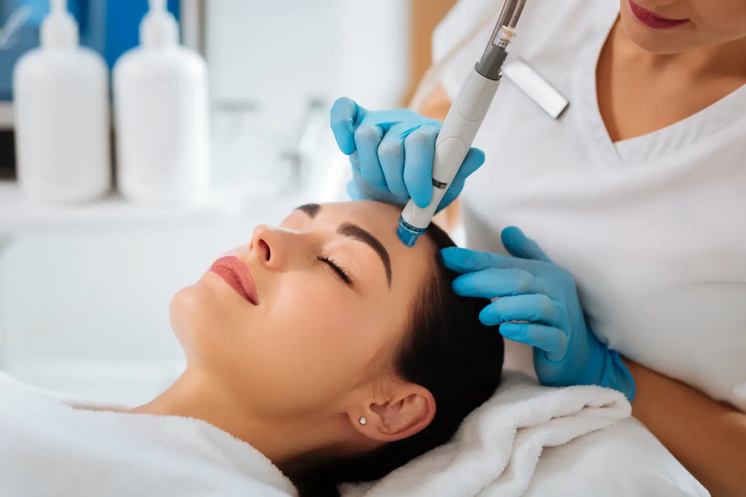 gloved hands using a handheld device on a woman's forehead during a facial treatment