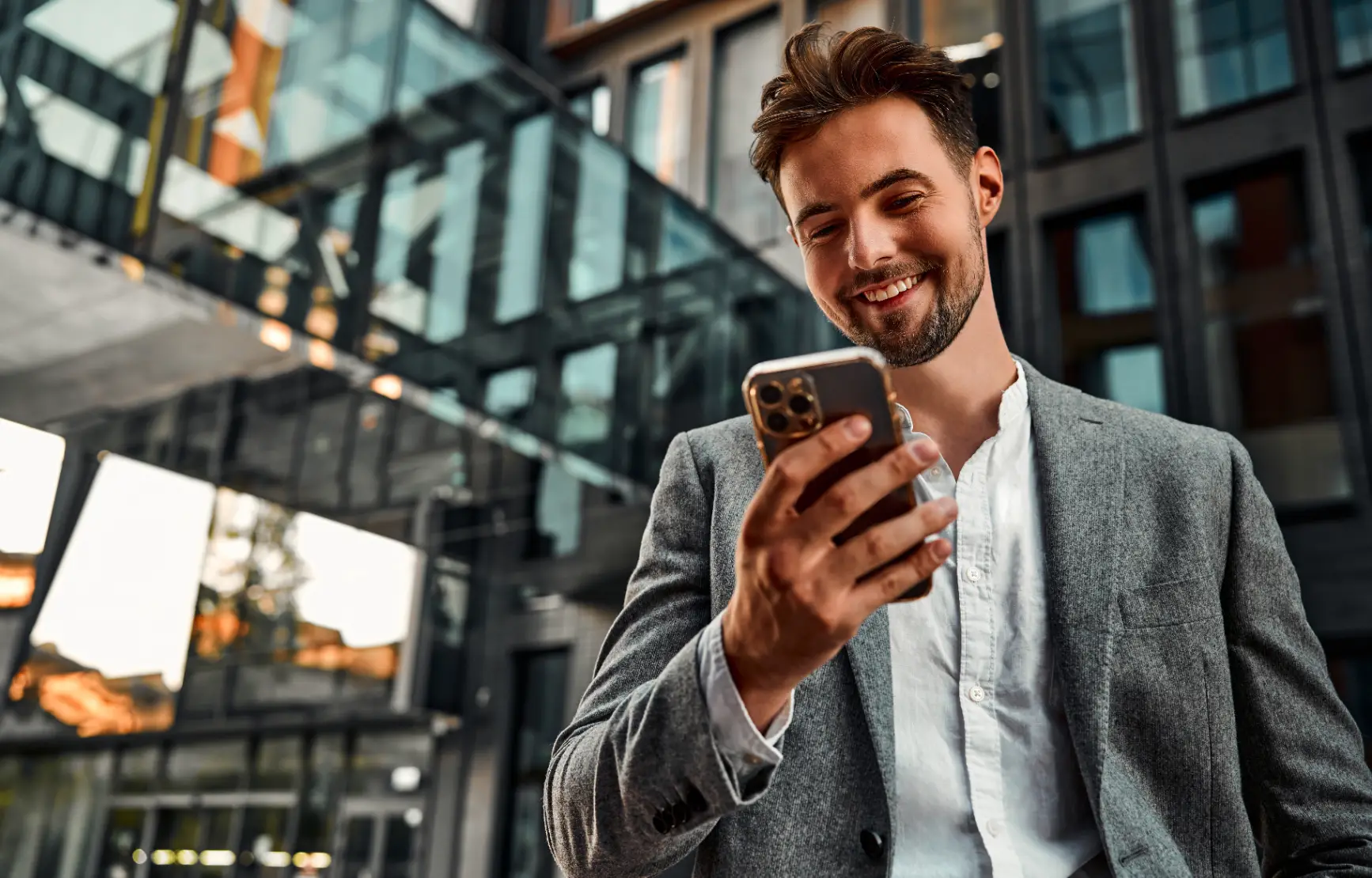 Smiling businessman looking at smartphone outside modern office building