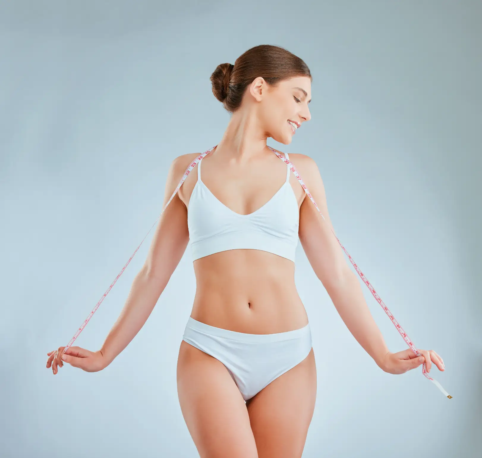 Woman in athletic wear holding a measuring tape around her upper body against a light background.