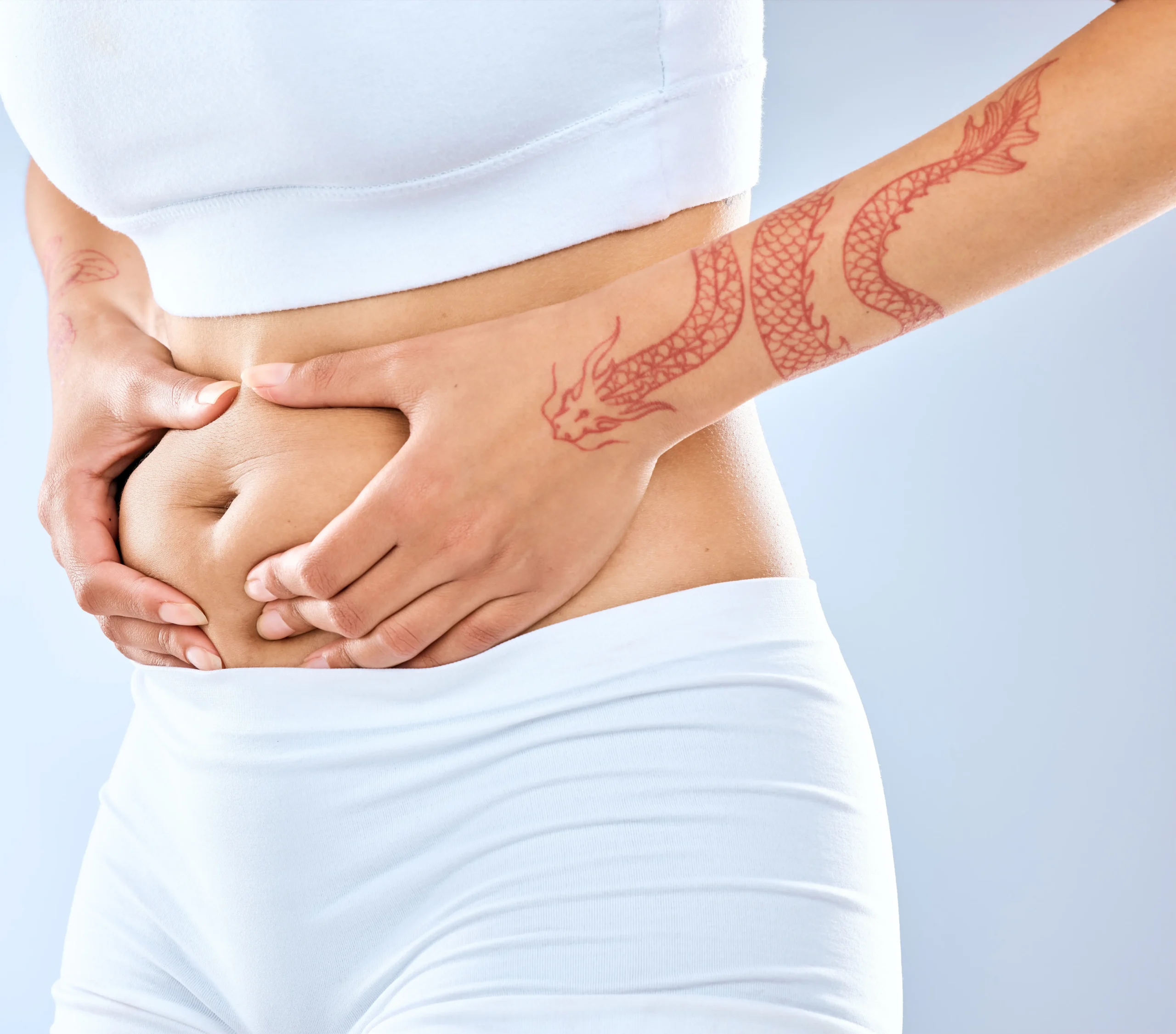 Close-up of hands gently pinching lower abdominal skin and fat while wearing athletic clothing.